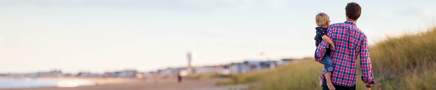 Man carries young son across a beach.